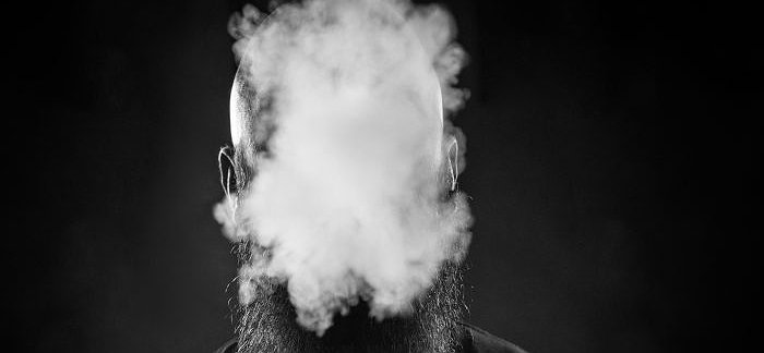 Un homme avec une barbe souffle un nuage de fumée