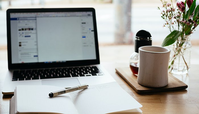 Un ordinateur portable, une carnet ouvert avec un stylo, un mug, et un petit vase avec des fleurs