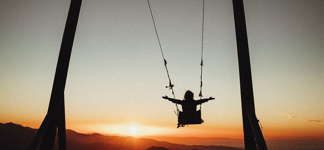 Un enfant est sur une balançoire au soleil levant
